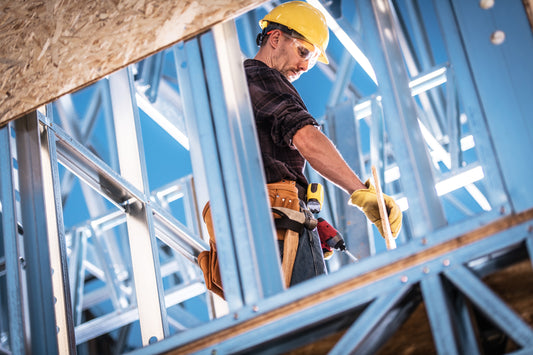 Construction worker in a yellow hard hat and work gloves working on a metal framed building 