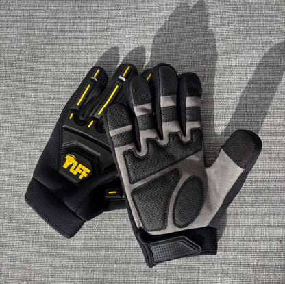 A pair of black and gray protective gloves with yellow accents, including a visible 'TUFF' logo on the back, laid flat on a gray textured surface.Safety Tuff gloves with finger guards (finger caps)