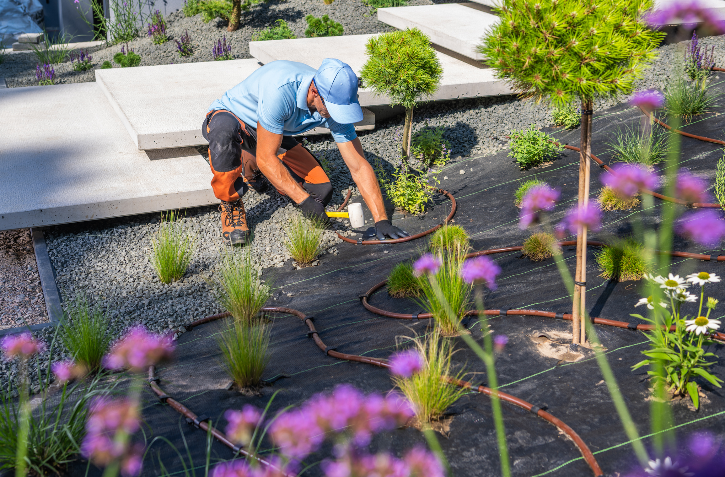 Landscaper using durable outdoor work gloves while trimming bushes, versatile gardening gloves and yard work gloves with reinforced palms and 500-lb finger guard protection.
